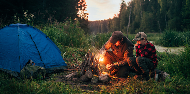 Father and son camping outdoors with a tent and campfire 